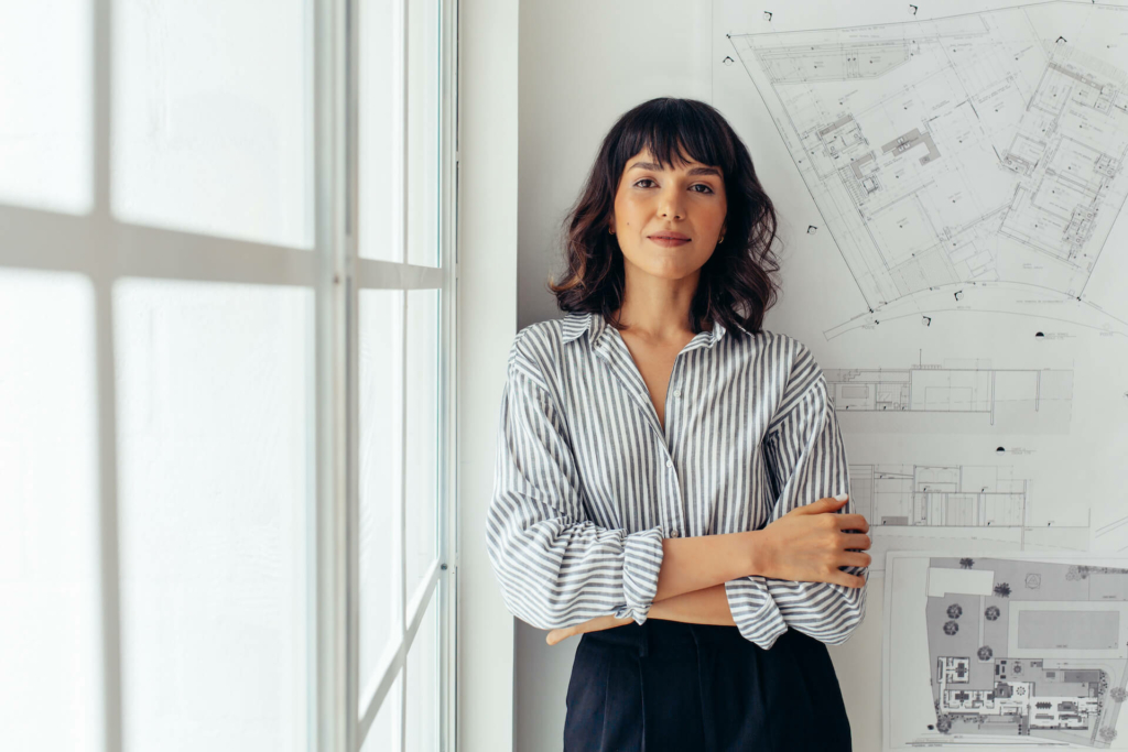 A woman standing in front of a blueprint with her arms crossed.